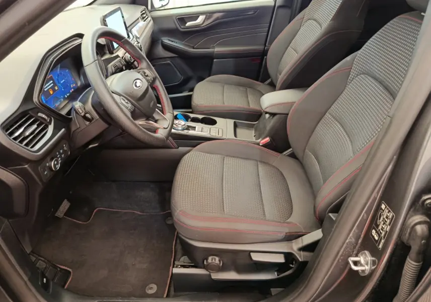 Vue intérieure côté conducteur du Ford Kuga gris clair 2024, sièges tissu avec surpiqûres rouges et tableau de bord numérique.