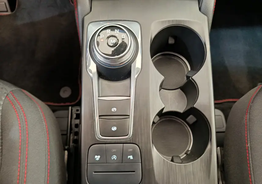Vue plongeante sur la console centrale noire du Ford Kuga 2024 avec molette de boîte auto et porte-gobelets.
