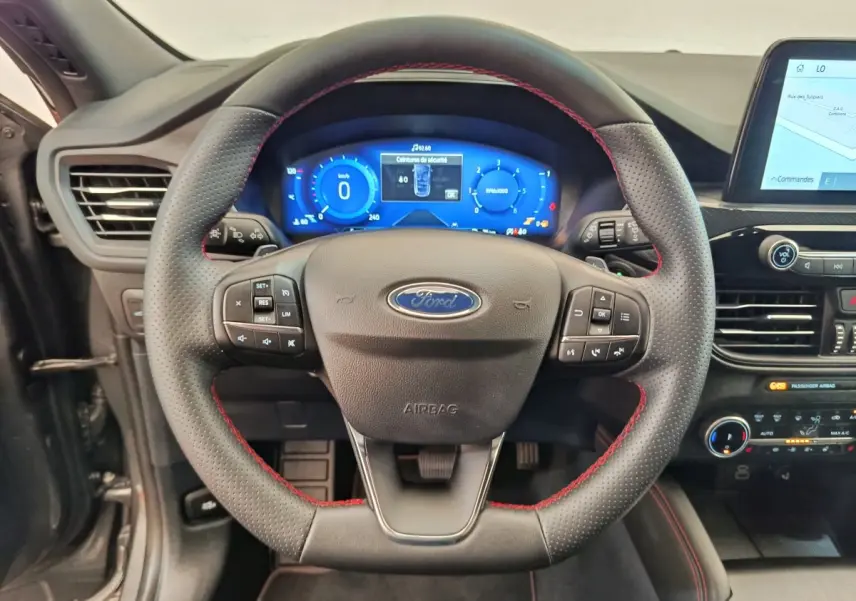 Vue rapprochée du volant noir avec surpiqûres rouges du Ford Kuga 2024, tableau de bord numérique et écran tactile visible.