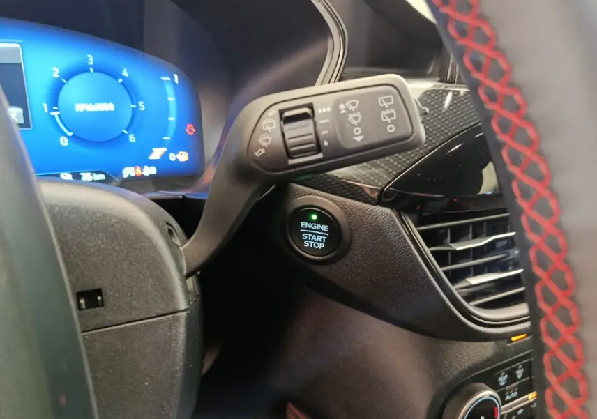 Détail intérieur du tableau de bord du Ford Kuga 2024, bouton démarrage et volant avec surpiqûres rouges visibles.