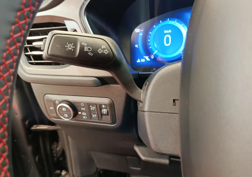 Gros plan sur le commodo gauche et le tableau de bord numérique bleu du Ford Kuga gris clair 2024, version St Line.