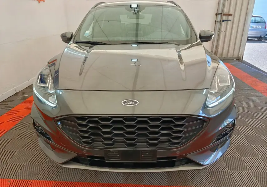 Vue frontale d'une Ford Kuga gris clair 2024 avec calandre hexagonale noire et phares LED allumés.