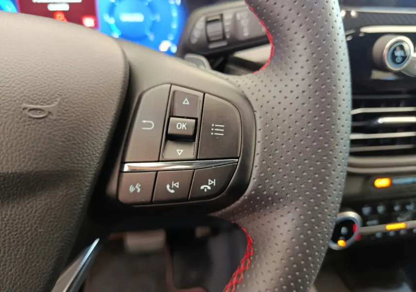 Gros plan sur le volant cuir noir à surpiqûres rouges du Ford Kuga 2024 avec commandes multifonctions visibles.