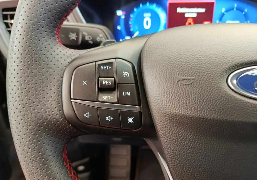 Gros plan sur le volant noir perforé avec surpiqûres rouges du Ford Kuga 2024, affichage numérique bleu en arrière-plan.