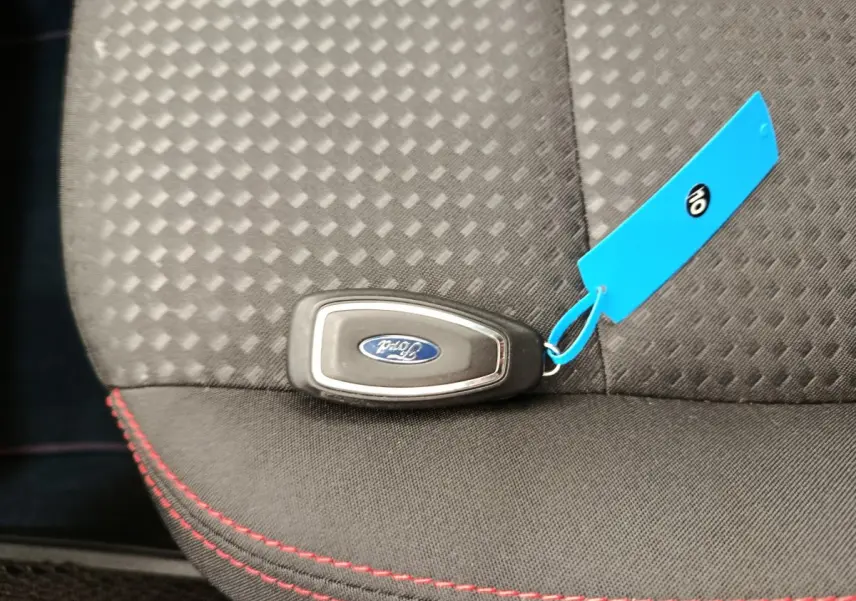 Gros plan sur la clé Ford posée sur un siège tissu gris foncé avec surpiqûres rouges visibles.