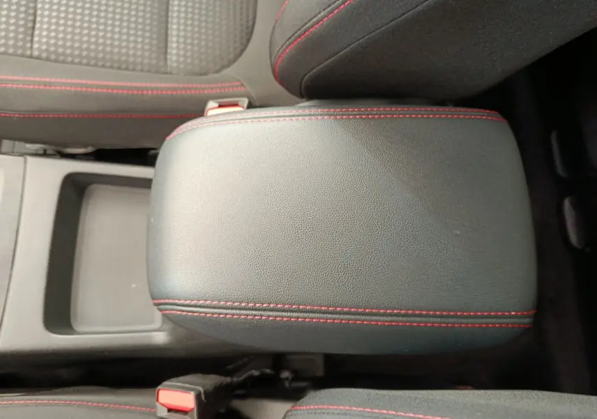 Gros plan sur l'accoudoir central noir avec surpiqûres rouges du Ford Kuga 2024, intérieur tissu gris et noir.