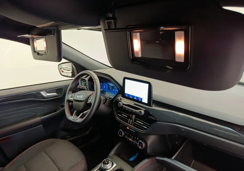 Intérieur du Ford Kuga 2024 en vue côté conducteur, tableau de bord moderne avec écran tactile et volant cuir noir.