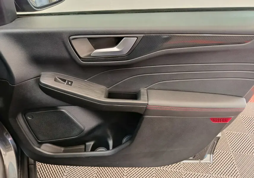 Gros plan sur la porte côté gauche du Ford Kuga gris clair, avec poignée argentée et surpiqûres rouges visibles.