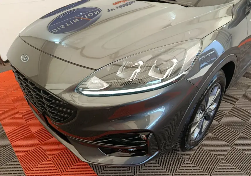 Vue 3/4 avant droit d'un Ford Kuga gris clair mettant en valeur ses phares LED et sa calandre noire sportive.
