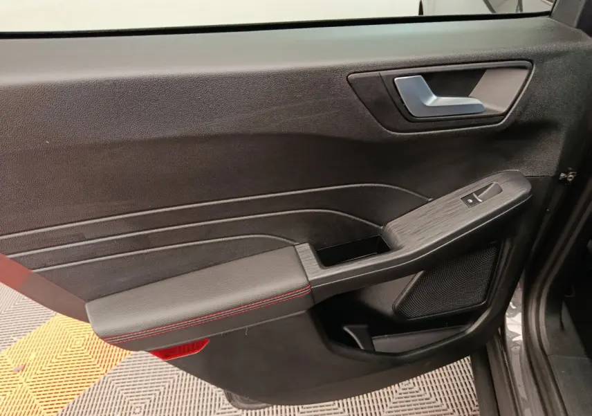 Gros plan sur la porte intérieure côté gauche du Ford Kuga gris clair, avec surpiqûres rouges et commande de fenêtre.