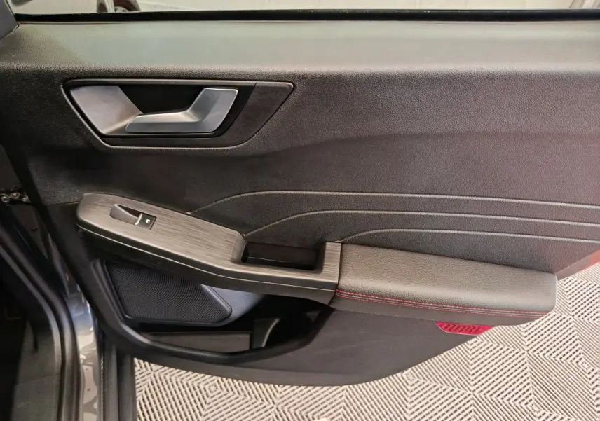 Gros plan sur la porte intérieure côté conducteur du Ford Kuga gris clair, avec accoudoir noir et surpiqûres rouges.