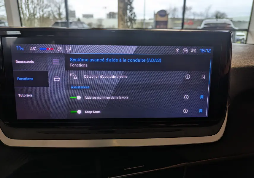 Écran tactile central affichant les aides à la conduite dans l’habitacle d’une Peugeot 208 noire, vue de face.