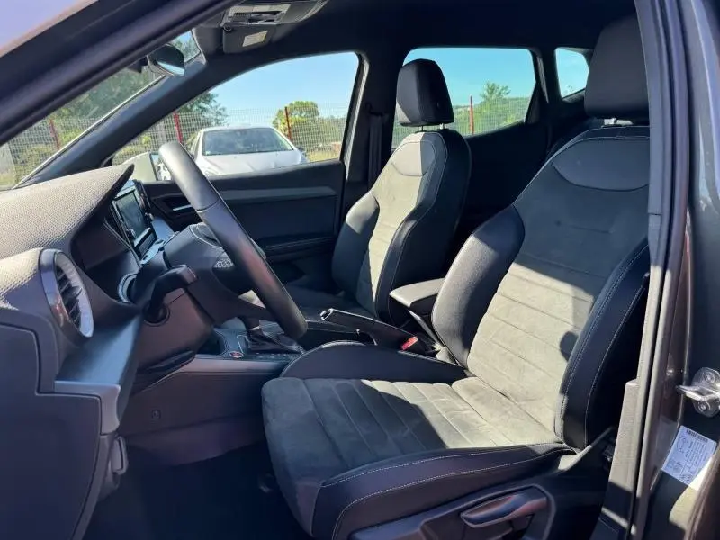 Vue intérieure côté conducteur du SEAT Arona noir 2025, sièges tissu gris Sano et volant cuir multifonction.