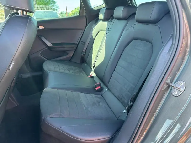 Vue intérieure côté droit sur la banquette arrière en tissu gris et cuir du SEAT Arona 2025 noir, avec ceinture de sécurité visible.