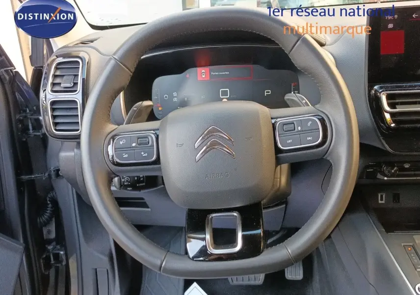 Vue intérieure centrée sur le volant noir du Citroën C5 Aircross 2025 avec tableau de bord numérique et commandes intégrées.