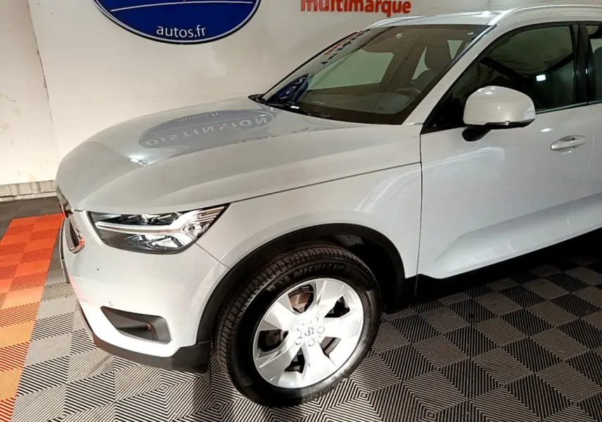 Vue 3/4 avant droit d'un Volvo XC40 gris clair avec jantes alliage et rétroviseur blanc dans un showroom.