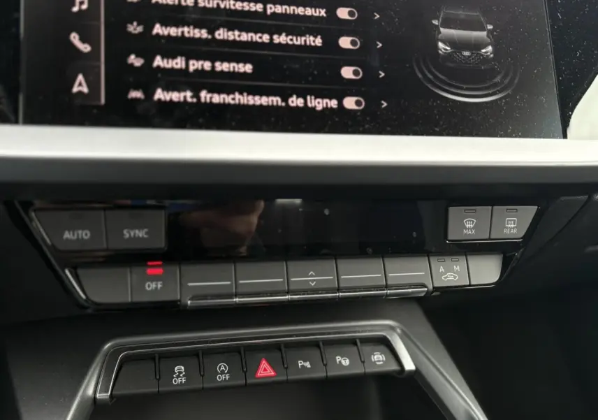 Vue rapprochée du tableau de bord de l'Audi A3 Berline 30 TFSI blanc, montrant les commandes climatisation et assistances.