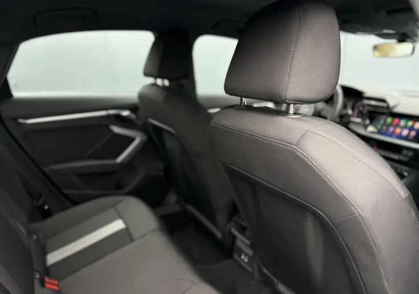 Vue intérieure arrière de l'Audi A3 Berline 2024 avec sièges tissu gris foncé et bande centrale claire.