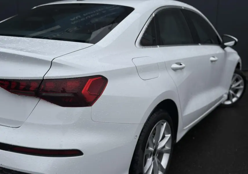 Vue 3/4 arrière droite d'une Audi A3 Berline 30 TFSI blanche Arkona avec feux arrière LED et jantes alliage 17 pouces.