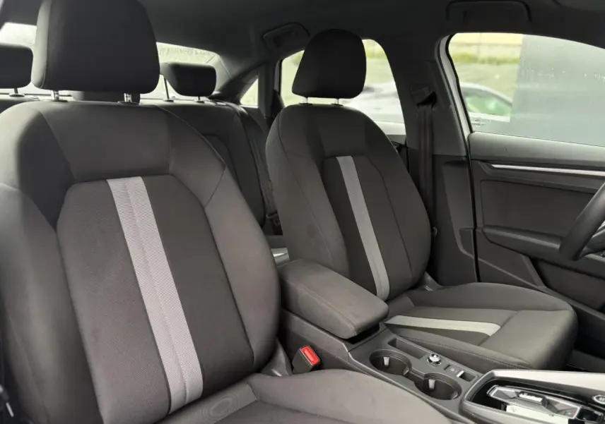 Vue intérieure montrant les sièges avant gris avec bande centrale claire et accoudoir coulissant de l'Audi A3 Berline 2024.