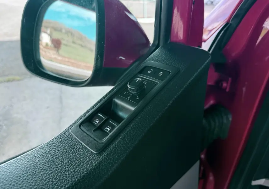 Vue rapprochée du panneau de commandes des vitres et rétroviseurs côté conducteur d’un Volkswagen Transporter rouge.