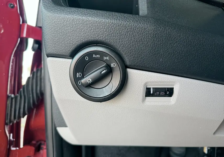 Gros plan sur le bouton de commande des phares dans l'habitacle d'un Volkswagen Transporter rouge, côté conducteur.