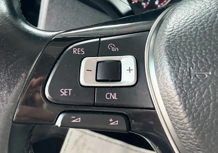 Gros plan sur les commandes du régulateur de vitesse sur le volant en cuir noir du Volkswagen Transporter rouge.