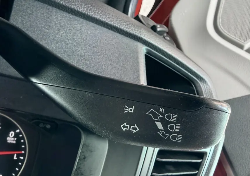 Gros plan sur la manette de clignotants noire à l'intérieur d'un Volkswagen Transporter rouge, côté conducteur.