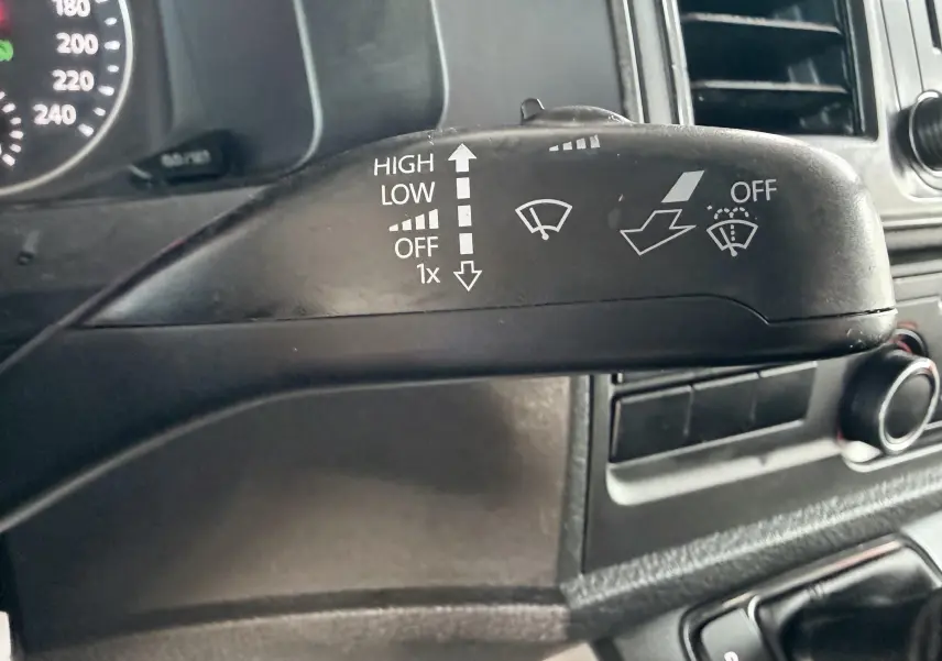 Gros plan sur la manette d’essuie-glace noire à gauche du volant dans l’habitacle du Volkswagen Transporter rouge.
