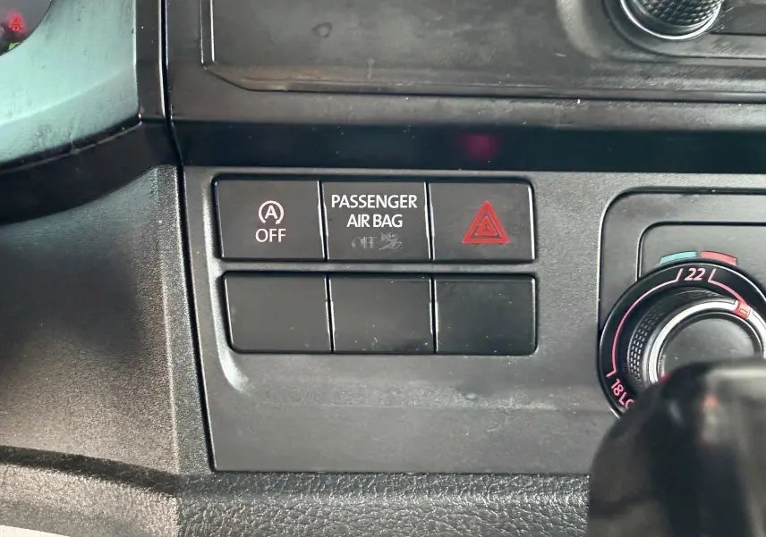 Gros plan sur les commandes du tableau de bord intérieur du Volkswagen Transporter rouge, avec bouton airbag passager et réglage clim.