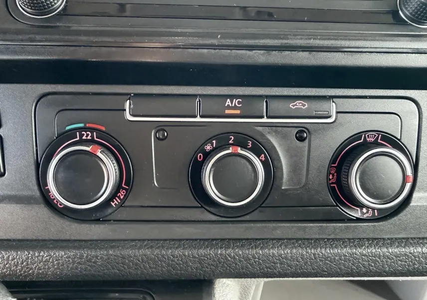Gros plan sur les commandes de climatisation du Volkswagen Transporter rouge, boutons rotatifs et fonction A/C visibles.