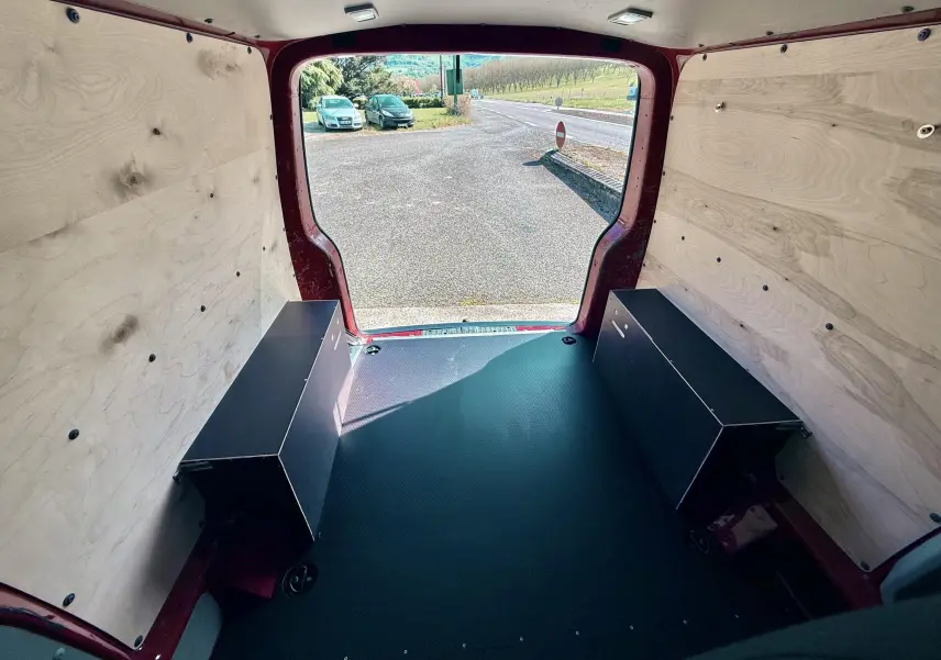 Vue intérieure arrière du Volkswagen Transporter rouge, montrant l’espace de chargement avec panneaux bois et sol noir antidérapant.
