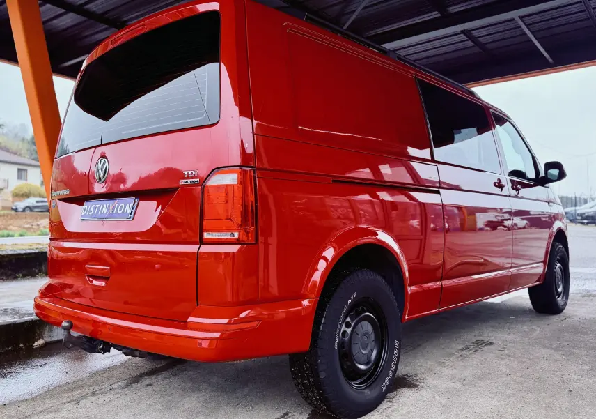 Vue 3/4 arrière droite d'un Volkswagen Transporter rouge, double cabine, avec jantes noires et vitres teintées.