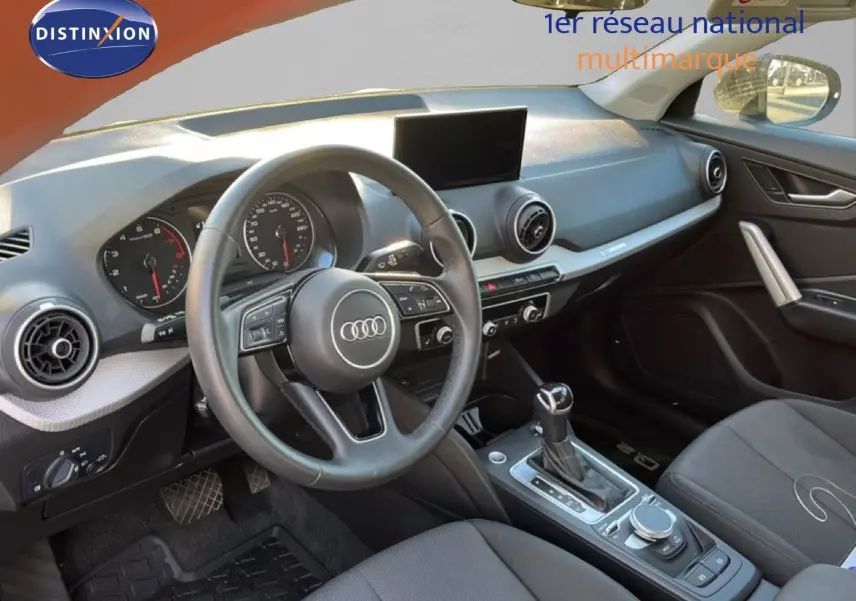 Intérieur de l'Audi Q2 35 TFSI 2023 vu côté conducteur, tableau de bord moderne avec volant multifonction et console centrale.