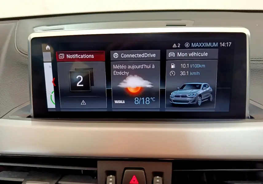 Écran central du tableau de bord montrant l’interface BMW avec météo, notifications et image du X2 blanc en vue avant.