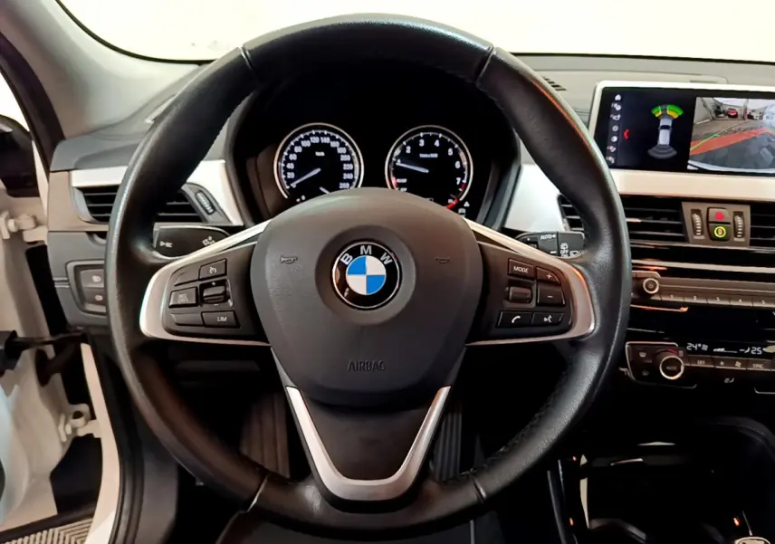 Vue intérieure centrée sur le volant cuir BMW d'un X2 blanc 2023 avec tableau de bord et écran multimédia.