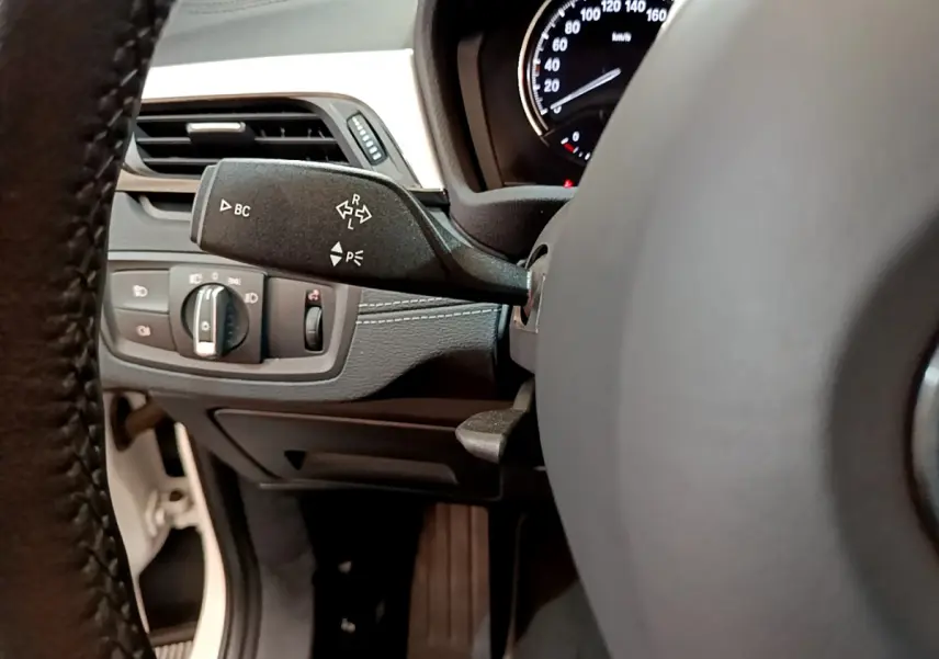 Gros plan sur la commande de clignotants et tableau de bord noir du BMW X2 blanc sDrive18i 2023, intérieur conducteur.