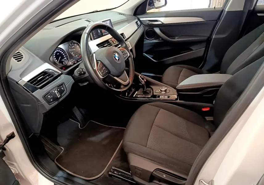 Vue intérieure côté conducteur du BMW X2 blanc 2023, avec tableau de bord moderne et sièges noirs en tissu.