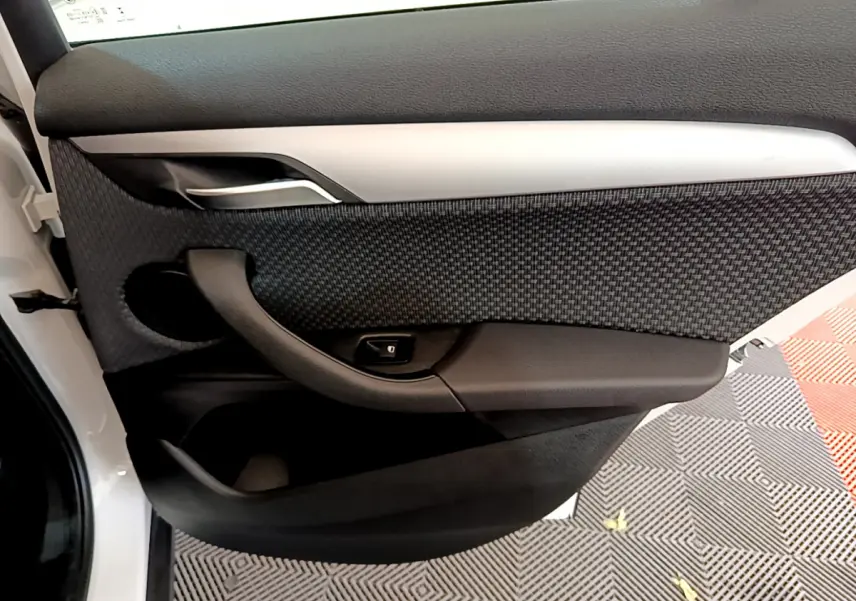 Gros plan sur la porte côté gauche blanche du BMW X2 2023, avec garniture noire texturée et poignée argentée.