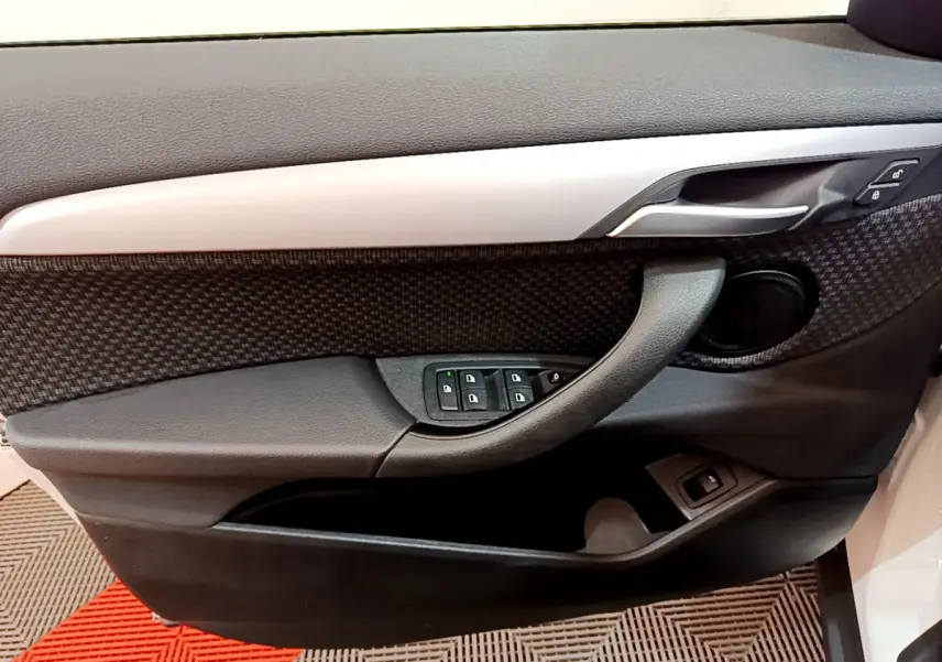 Vue rapprochée de la porte côté gauche d’une BMW X2 blanche, avec commandes électriques et garniture noire texturée.