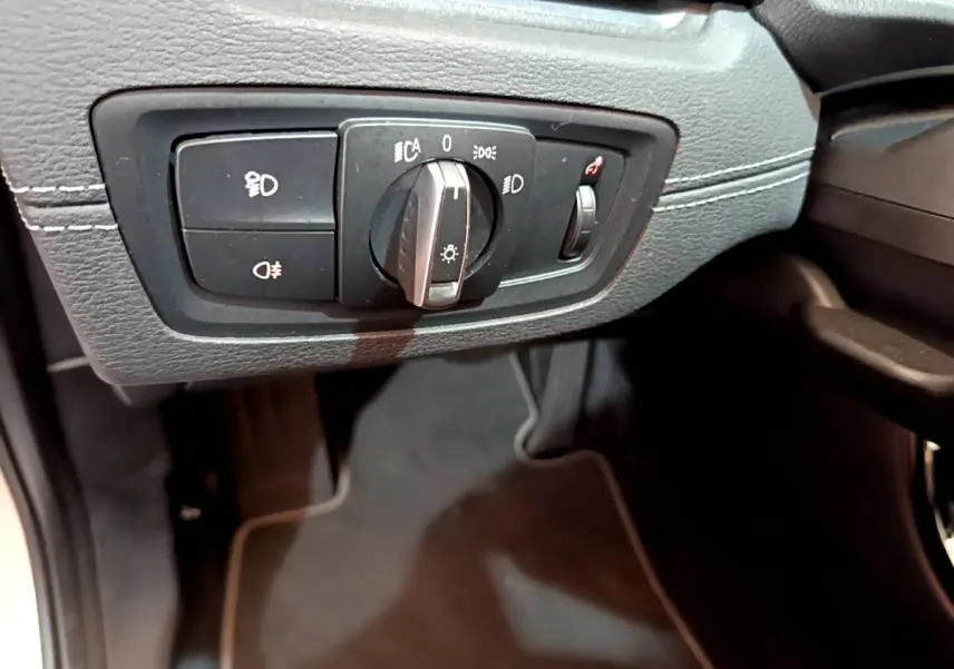 Gros plan sur le bouton de commande des phares noir avec molette, côté gauche du tableau de bord d'une BMW X2 blanche.