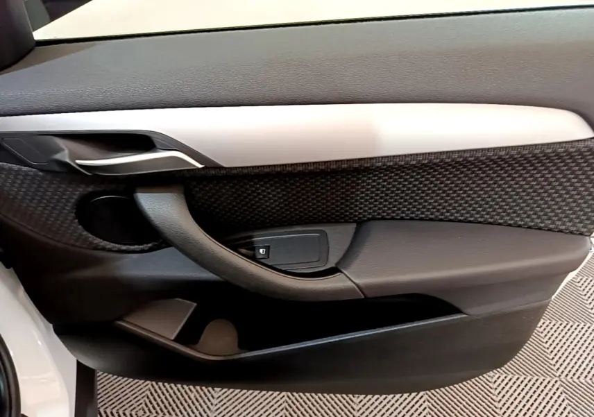 Détail de la porte côté gauche intérieure du BMW X2 blanc 2023 avec poignée noire et insert décoratif gris.