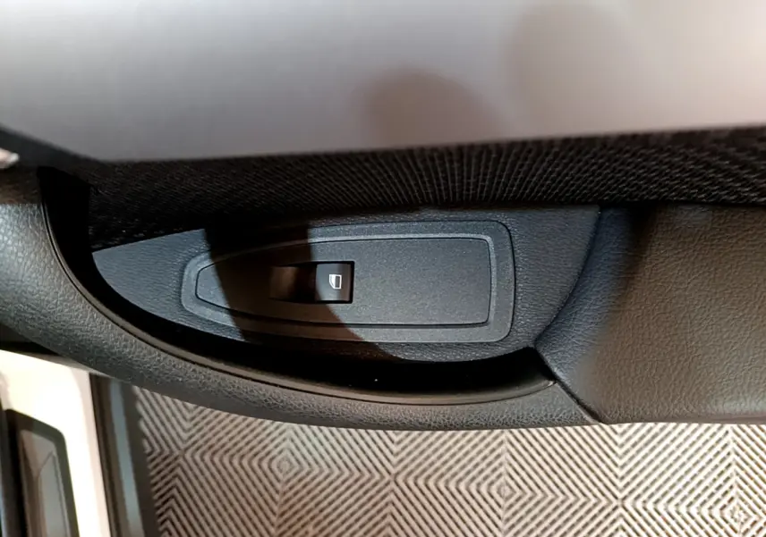 Bouton de commande de lève-vitre côté conducteur dans l'habitacle noir du BMW X2 blanc 2023.