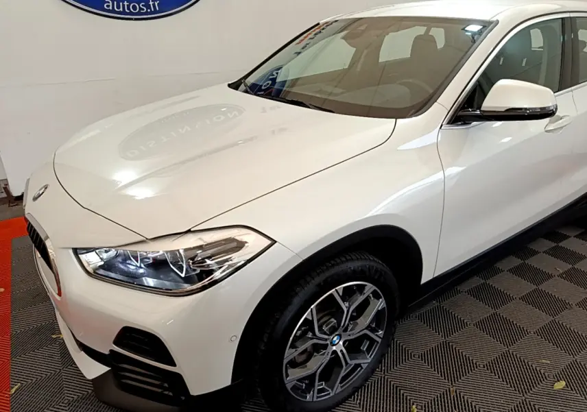 BMW X2 sDrive18i blanc en 3/4 avant droit, avec phares LED allumés et jantes alliage distinctives