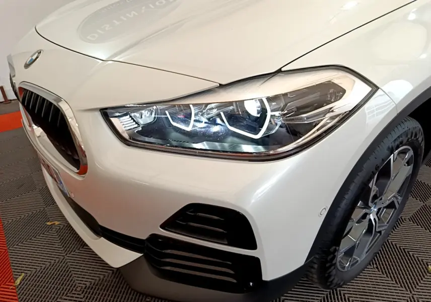 Gros plan sur l'avant droit blanc d'un BMW X2 2023, mettant en valeur le phare LED et la calandre caractéristique.