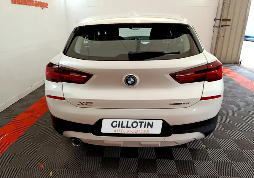 Vue arrière d'un BMW X2 blanc sDrive18i avec feux LED et sortie d'échappement visible en garage.