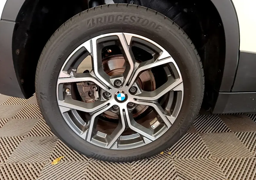 Gros plan sur la roue avant droite d’un BMW X2 blanc 2023 avec jante alliage et pneu Bridgestone visible.
