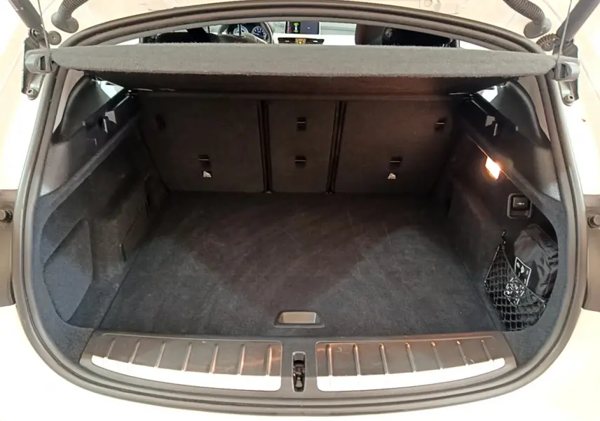 Coffre ouvert vu de l'arrière d'un BMW X2 blanc 2023, espace de chargement propre avec filet latéral et éclairage intérieur.
