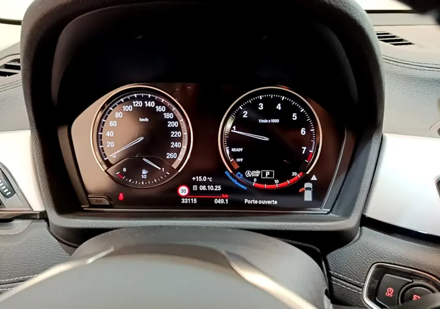 Tableau de bord numérique de BMW X2 blanc 2023, affichage vitesse et compte-tours avec indications de température et porte ouverte.