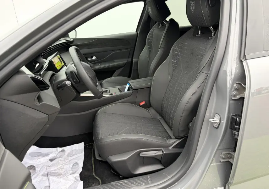 Vue intérieure côté conducteur de la Peugeot 308 gris selenium, sièges sport noirs avec surpiqûres vertes et tableau de bord moderne.